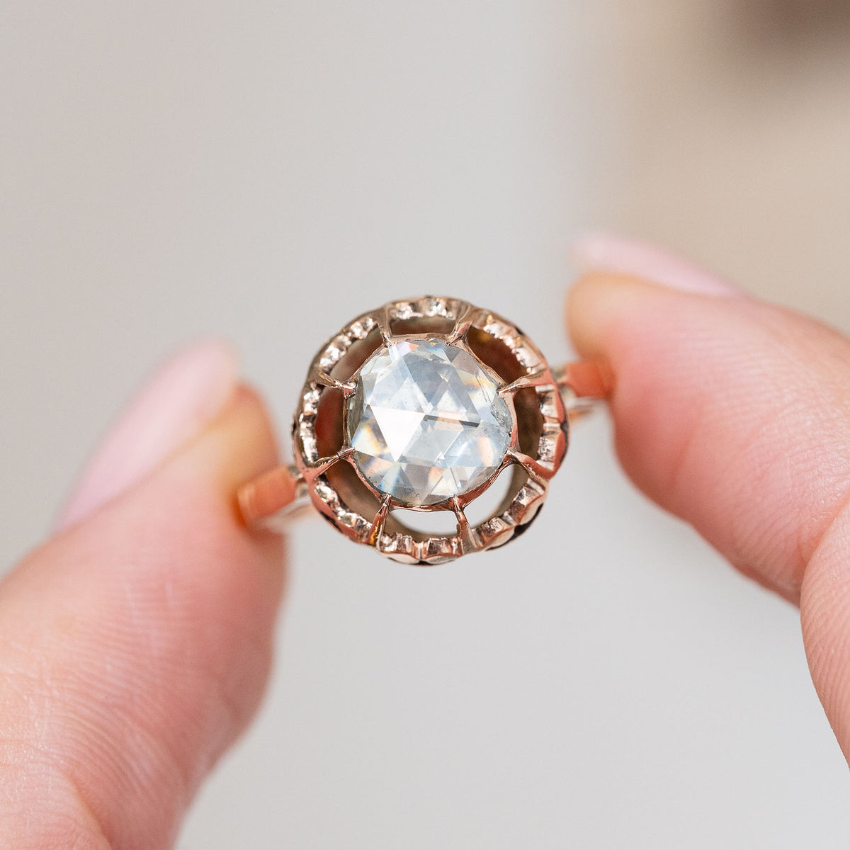 Held between the fingers, the antique solitaire displays the diamond’s broad rose-cut facets and handcrafted open gold surround.