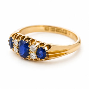 An Antique, Edwardian sapphire and diamond five-stone engagement ring in yellow gold on a white background turned at an angle showcasing the shoulders.