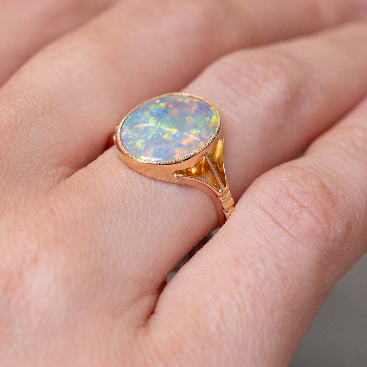 A close-up of an antique, Edwardian era oval opal single stone ring with decorative split shoulders mounted in yellow gold worn on the finger and photographed from a side angle showing off the style of setting and profile of the ring when worn on the hand.