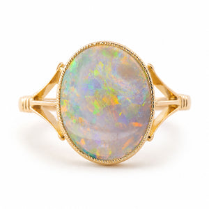 An Antique, Edwardian era oval opal solitaire ring with split yellow gold shoulders and a decorative rub-over setting shown against a white background.