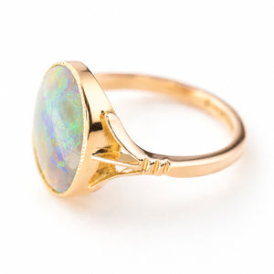An image of an antique, Edwardian era opal ring in yellow gold shown up close and at an angle to show the decorative split shoulders and gold band against a plain white background.