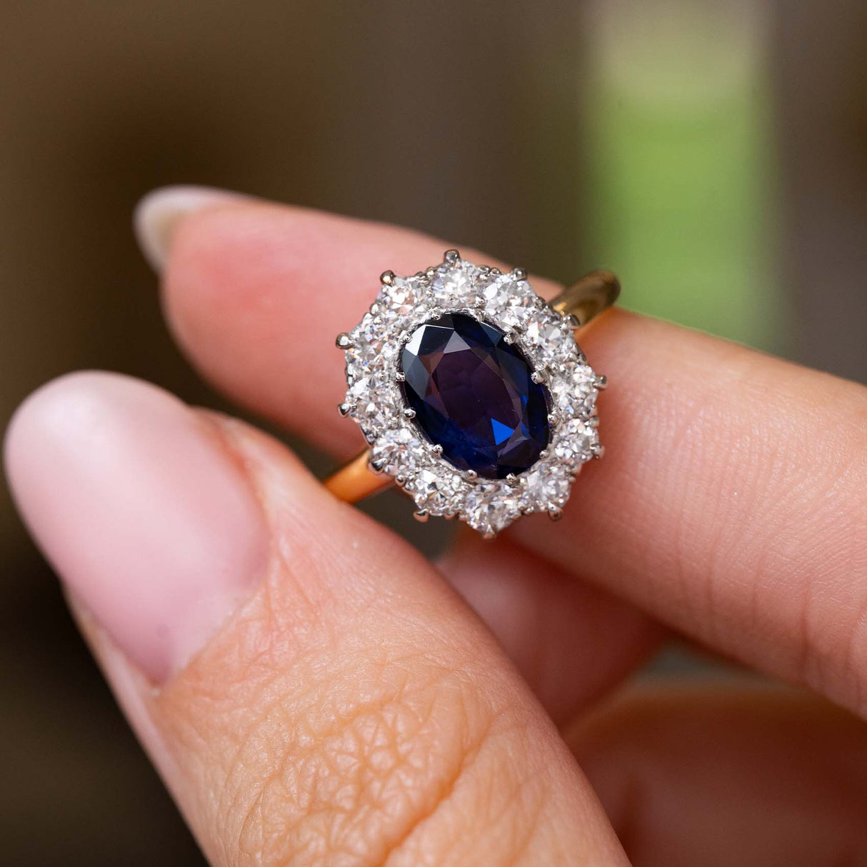 A close-up of a hand holding a Vintage, 1940s blue sapphire and diamond cluster engagement ring with a yellow gold band. 