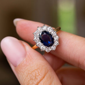 A close-up of a hand holding a Vintage, 1940s blue sapphire and diamond cluster engagement ring with a yellow gold band. 