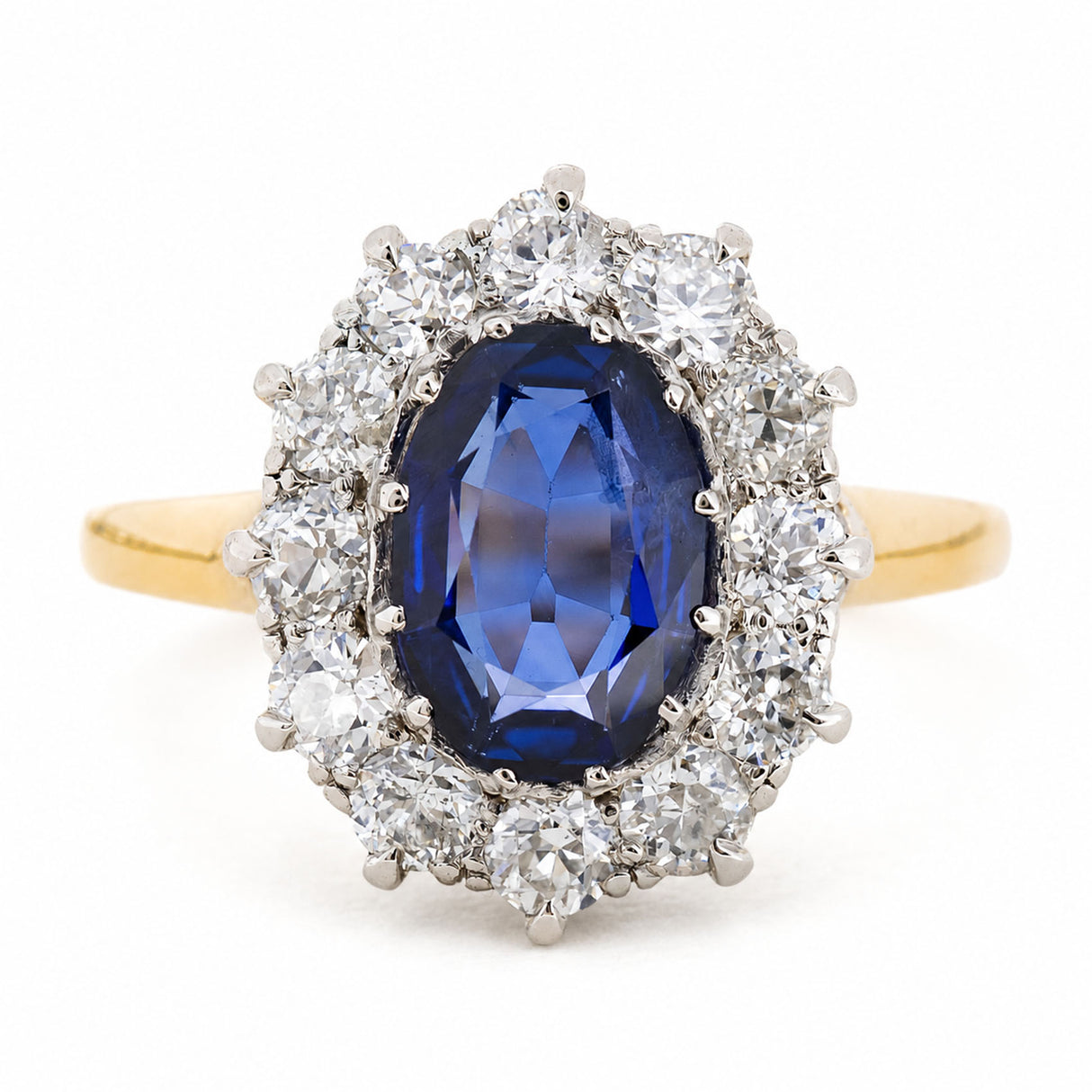 A Vintage, 1940s blue sapphire and diamond cluster engagement ring with a yellow gold band, against a plain white background.