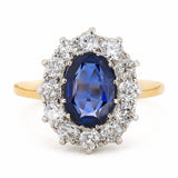 A Vintage, 1940s blue sapphire and diamond cluster engagement ring with a yellow gold band, against a plain white background.