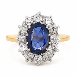 A Vintage, 1940s blue sapphire and diamond cluster engagement ring with a yellow gold band, against a plain white background.