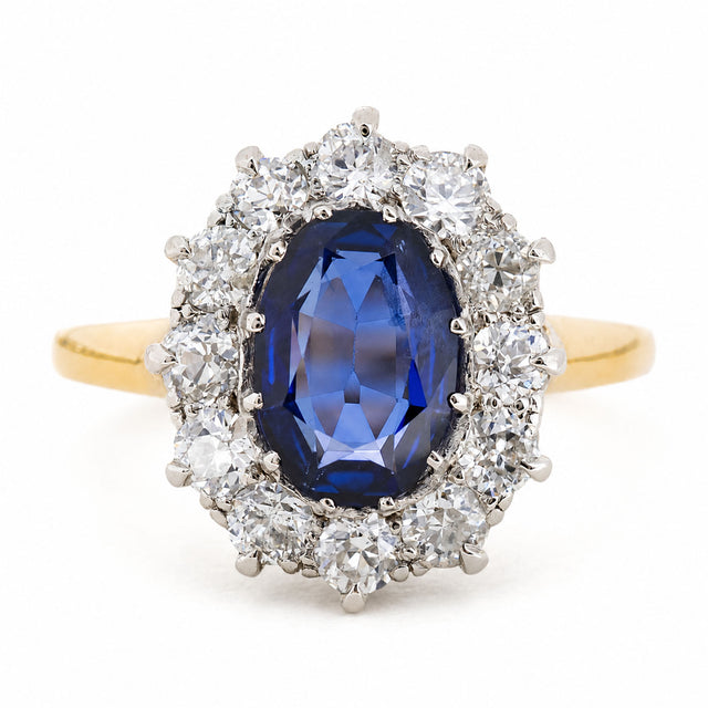 A Vintage, 1940s blue sapphire and diamond cluster engagement ring with a yellow gold band, against a plain white background.