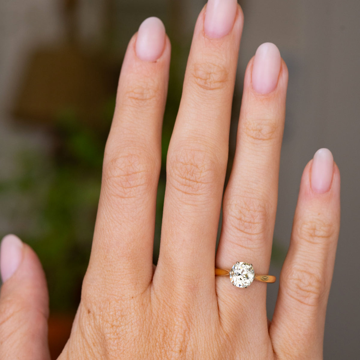 A close-up of a hand wearing a yellow gold Antique, Edwardian yellow tinted diamond solitaire engagement ring to show scale
