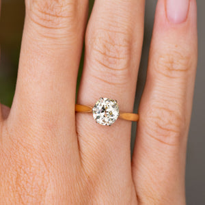 A close up detail of an Antique, Edwardian yellow tinted diamond solitaire engagement ring in yellow gold worn on the hand