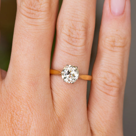 A close up detail of an Antique, Edwardian yellow tinted diamond solitaire engagement ring in yellow gold worn on the hand