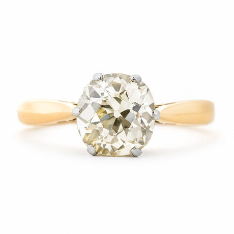 A front profile of an antique, Edwardian yellow tinted cushion-shaped old-cut diamond solitaire engagement ring with a yellow gold band.