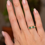 An Antique, Victorian emerald and diamond five-stone engagement ring worn on the hand and shown from a distance to show off scale.