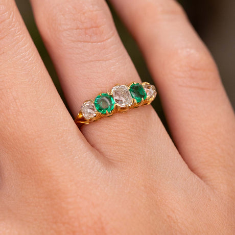 A close up detailed image of a hand wearing an Antique, Victorian emerald and diamond five-stone engagement ring in yellow gold.