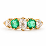 A yellow gold ring featuring three oval-cut emeralds and three old-cut diamonds, in a five stone engagement ring seen against a white background. 