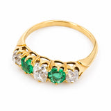 A Victorian emerald and diamond five-stone engagement ring in yellow gold shown on a white background from an elevated angle to show off the shank and pierced gallery.