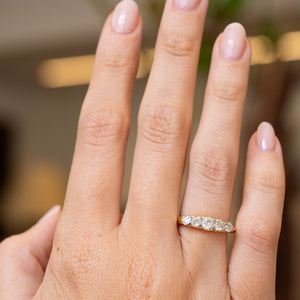 A close-up of a hand wearing a yellow gold Antique Victorian diamond five-stone engagement ring, with a softly blurred indoor background.