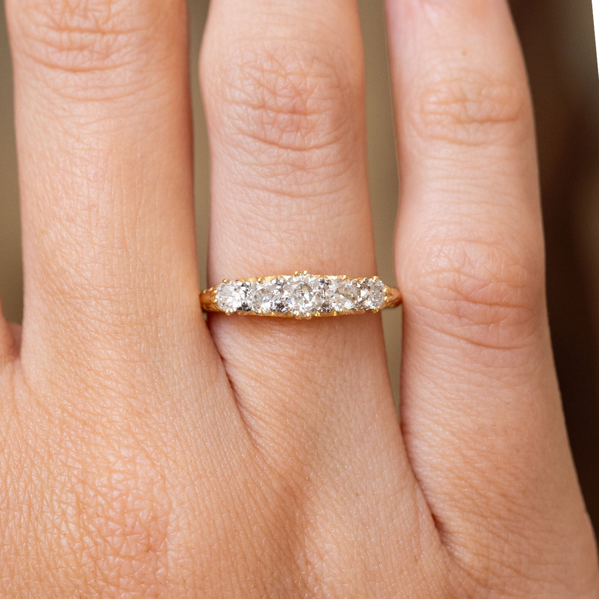 A close up image of an Antique, Victorian diamond five-stone engagement ring, shown worn on a wedding finger.