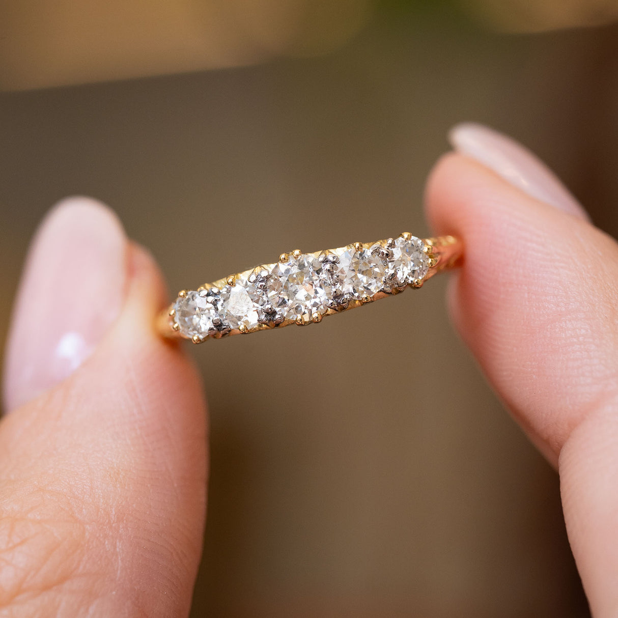 A close-up of an Antique yellow gold Victorian five-stone diamond engagement ring held between two fingers. 