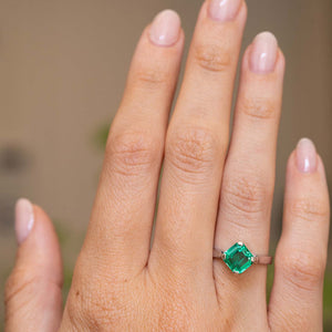 A close-up of a hand wearing a Vintage, 1990s square-cut emerald solitaire unique engagement ring in white gold. 