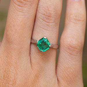A close-up of a Vintage 1990s engagement ring worn on a wedding finger, featuring a square-cut emerald in a white gold setting. 