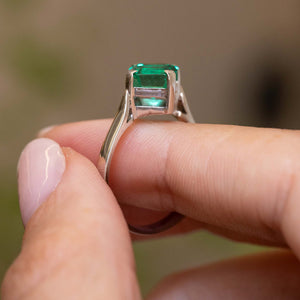 A close-up of a hand holding a Vintage, 1990s emerald solitaire engagement ring, showcasing the side profile and white gold setting of the emerald and band.  