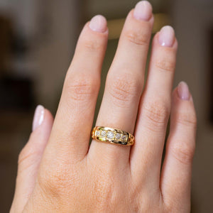 A close-up of a yellow gold Antique, Victorian diamond five-stone engagement ring worn on the hand shown from a distance to show off the proportions against a blurred grey background.