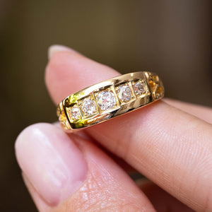 A yellow gold Antique, Victorian diamond five-stone engagement ring held between fingers to show scale and seen against a blurred background.