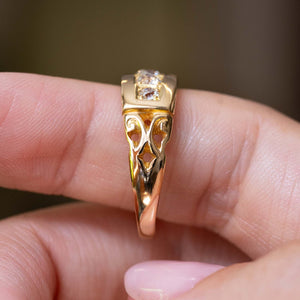 A close-up image of an Antique, Victorian diamond five-stone yellow gold engagement ring with a ornate carved shoulders shown resting on a person's fingers.