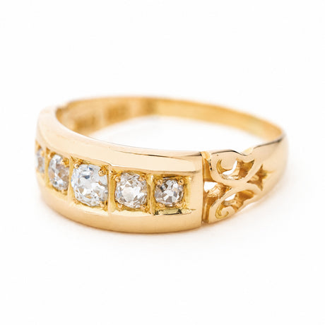 A yellow gold Antique, Victorian diamond five-stone engagement ring photographed on a white background and seen from the side to showcase the decorative carved shoulders.