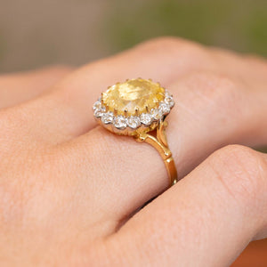 A yellow sapphire and diamond cluster engagement ring in yellow gold on a person's hand, showing the setting style and gallery