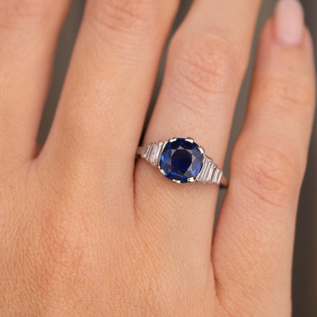 A close-up of a hand wearing a platinum Antique, Art Deco blue sapphire and diamond engagement ring.