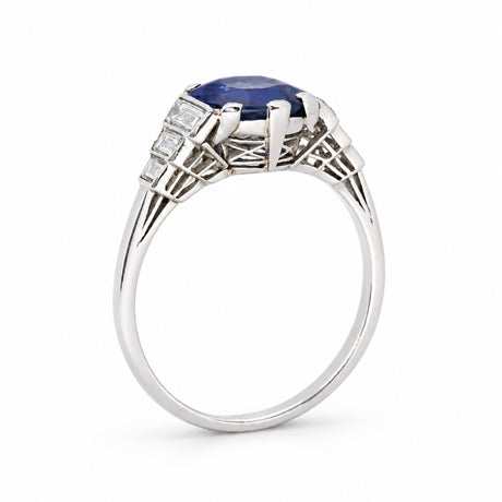 An antique engagement ring in platinum with a blue sapphire at the centre flanked by diamonds on the shoulders and an intricately carved gallery