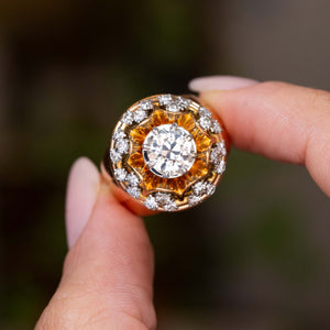 A close-up of a hand holding a Vintage, 1960s French old cut diamond cocktail ring featuring a cluster design against a blurred green background.