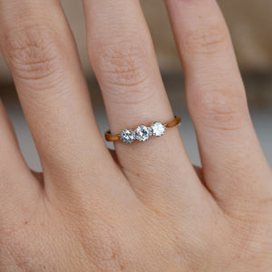 Close-up of three round old-cut diamonds set in platinum on a yellow gold band, worn on a finger.