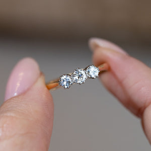 Hand-held close-up of the three sparkling old-cut diamonds, featuring a larger central stone flanked by two smaller diamonds.