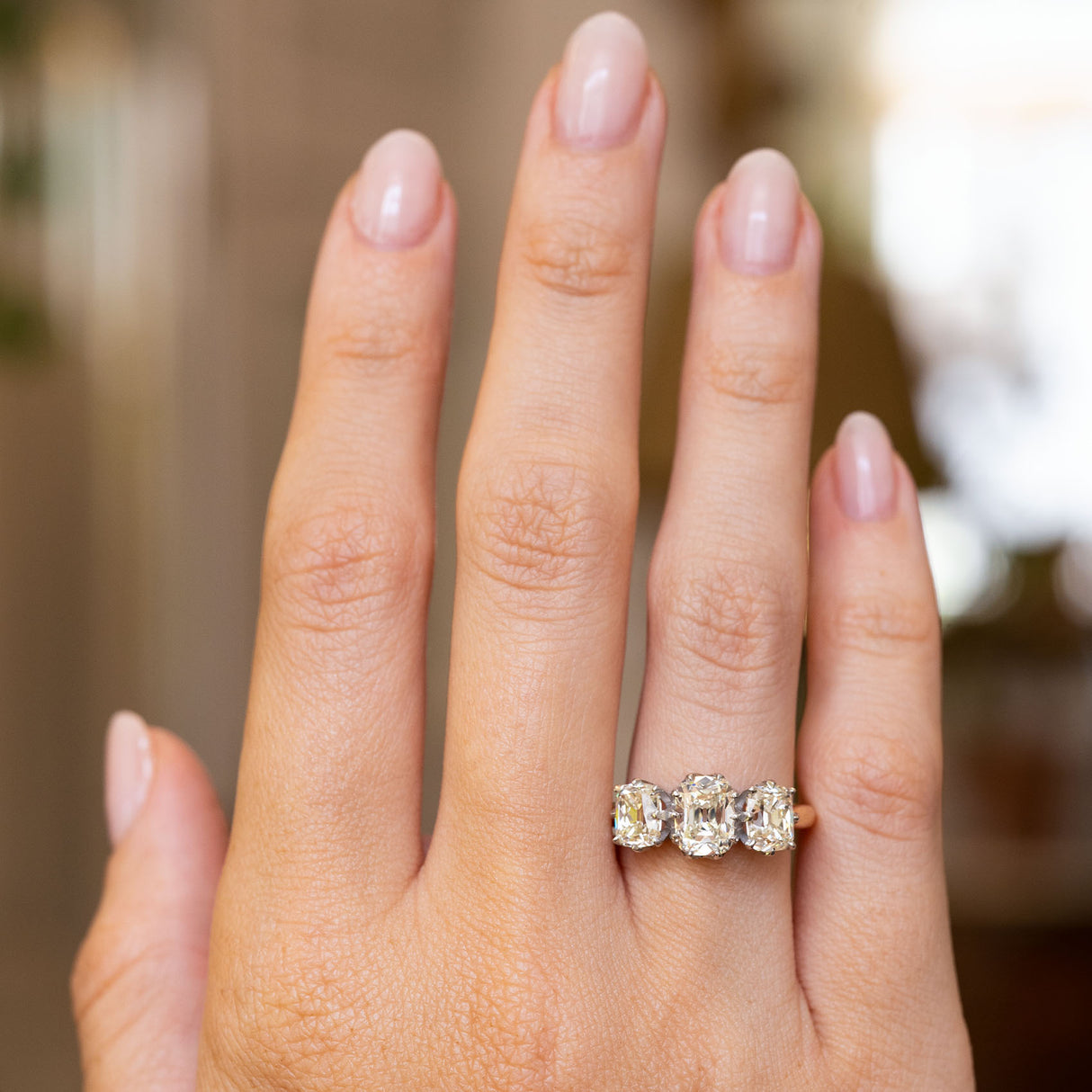 An image of a diamond trilogy engagement ring being worn on the hand and shown at a distance against a softly blurred background