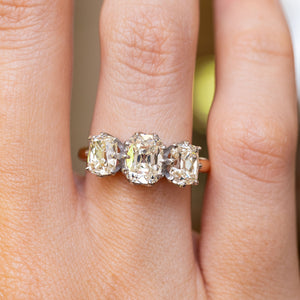 a close up of a vintage diamond engagement ring with three stones on a yellow gold band worn on the hand 