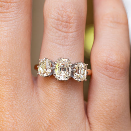 a close up of a vintage diamond engagement ring with three stones on a yellow gold band worn on the hand 