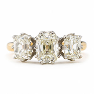 Antique old mine cut diamond trilogy ring on  yellow gold band against a plain white background.