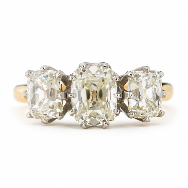 Antique old mine cut diamond trilogy ring on  yellow gold band against a plain white background.