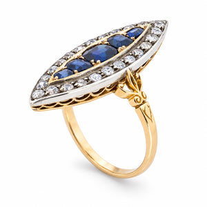 A sculptural three-quarter view reveals the elongated sapphire arrangement, diamond-set silver surround and engraved yellow gold shoulders.