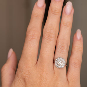 A hand wearing a platinum Antique, Edwardian diamond cluster engagement ring.
