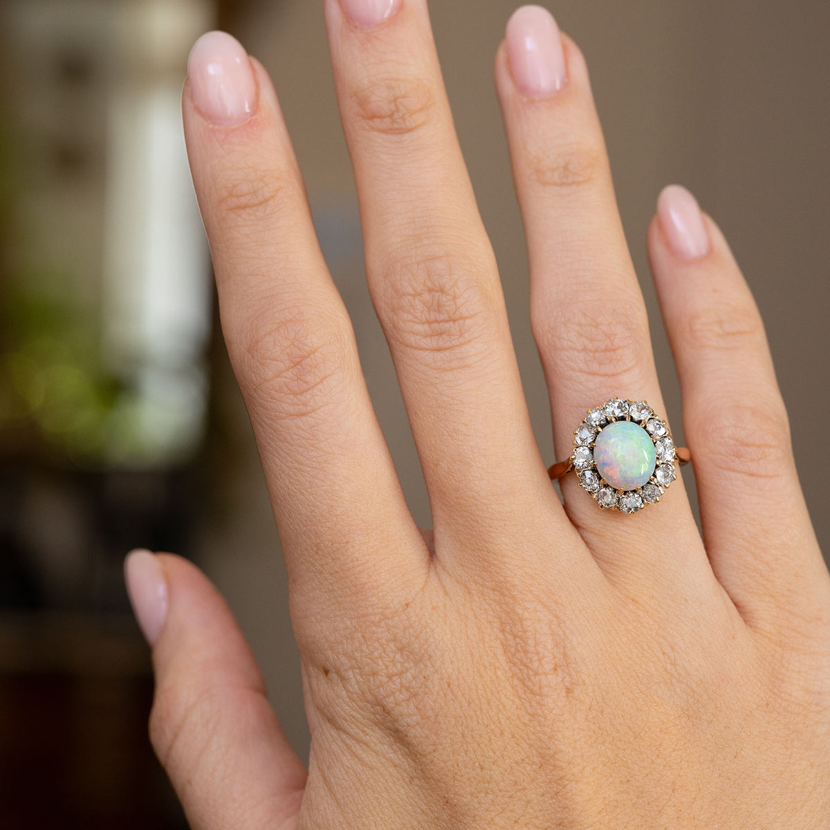 Antique opal and diamond ring worn on the hand, showing the statement cluster’s proportions and flashes of green, pink and yellow.