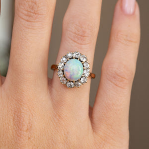Detailed hand shot highlighting the luminous oval opal, antique diamond surround and warm yellow gold setting.