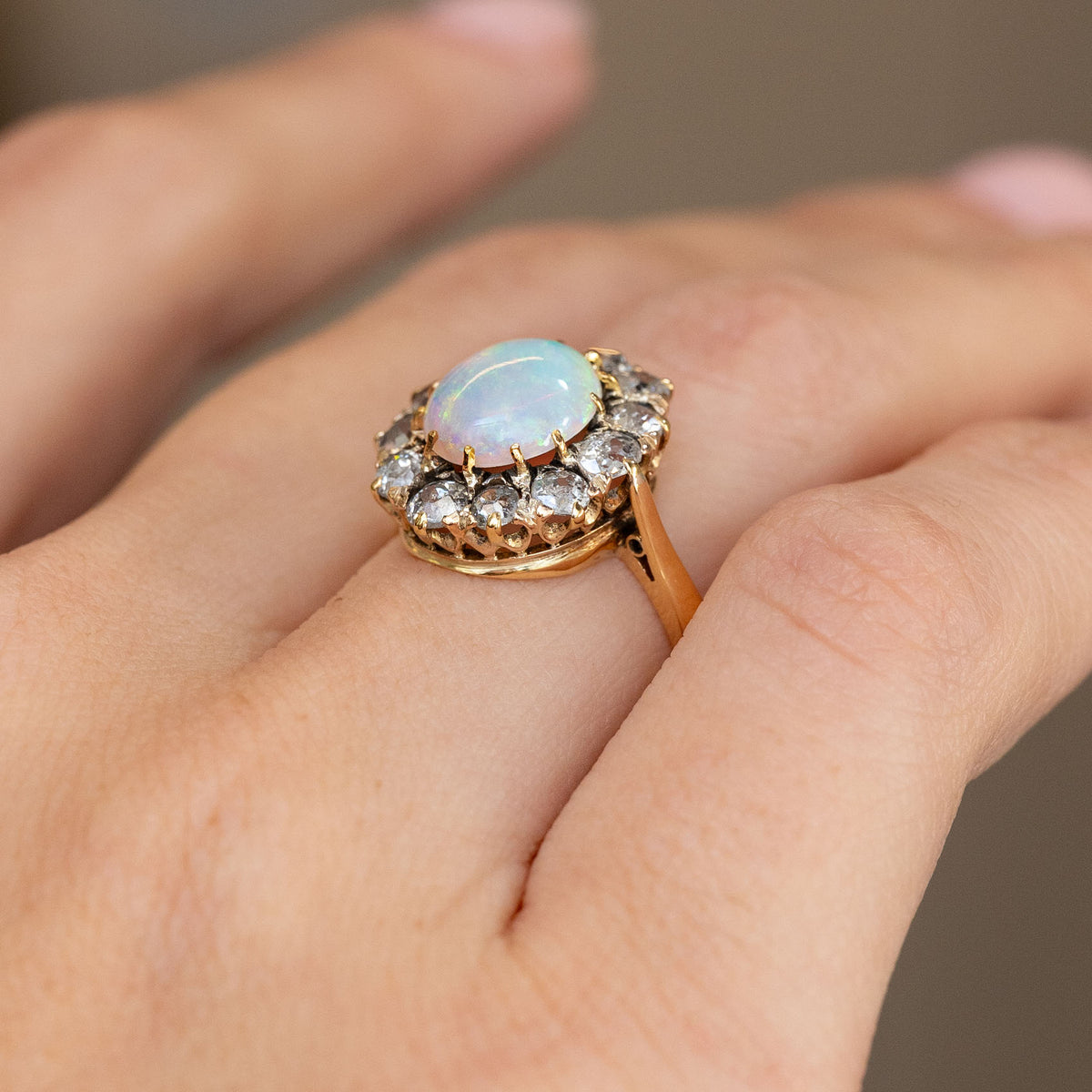 Side-angled view of the antique opal ring being worn, showcasing its raised cluster setting and decorative yellow gold gallery.