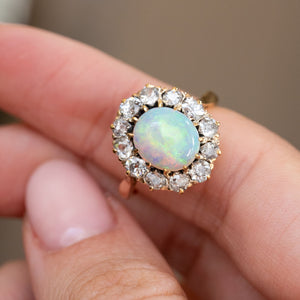Handheld macro view of the iridescent opal cabochon encircled by sparkling antique-cut diamonds.