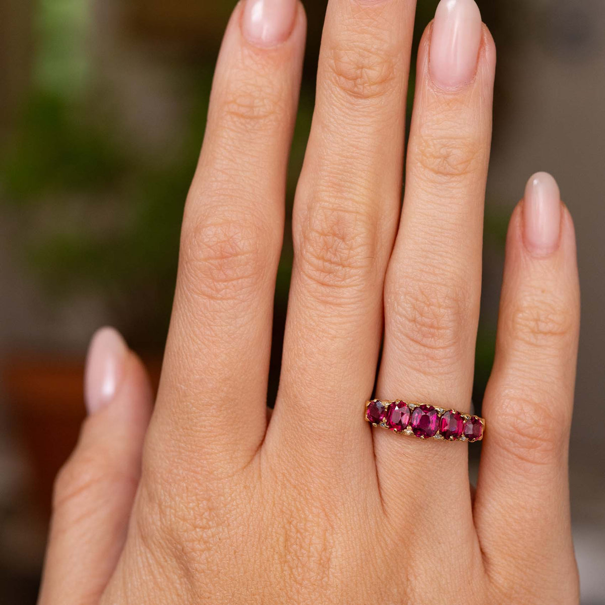 A hand wearing an Antique, Victorian ruby and diamond five-stone engagement ring in yellow gold shown for scale.