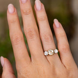 A hand wearing an Antique, Edwardian brown diamond three-stone engagement ring in yellow gold with platinum settings.