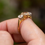 A close-up of a yellow gold Antique, Edwardian brown diamond trilogy engagement ring worn on a person's finger shown from the side to display the gallery and shoulders.
