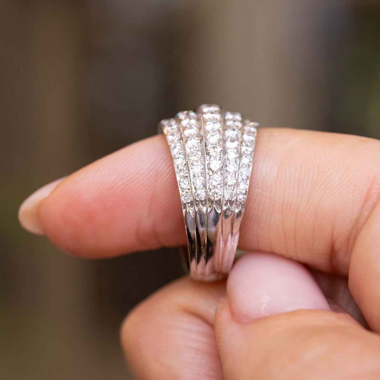 A close-up of a hand wearing a A Vintage, 1950s diamond bombe cocktail ring in white gold held up to show the shoulders and side of the ring